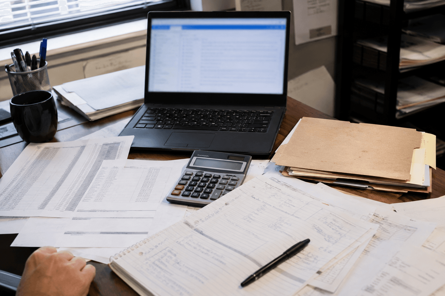 Freight rate sheets, calculator, folders, and laptop spread across a busy pricing desk